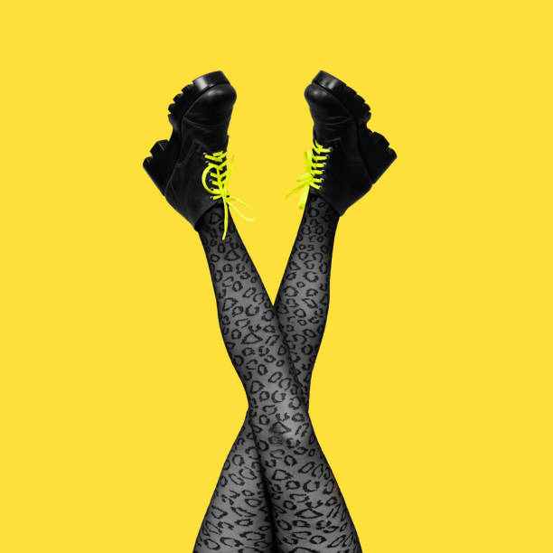 nuevas botas femeninas grises con cordones amarillos brillantes en largas piernas de mujer cruzadas delgadas en medias grises aisladas sobre fondo amarillo. bandera cuadrada - punk fotografías e imágenes de stock