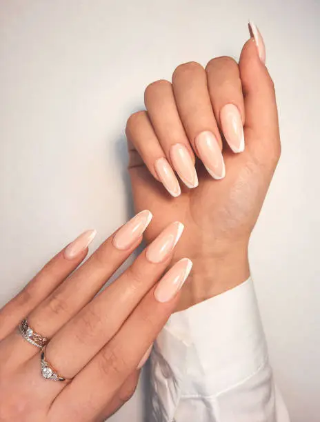 Gentle camouflage gel polish on long square nails with a French design. Hands with a professional manicure in a shirt. Trendy nail coating with French design.