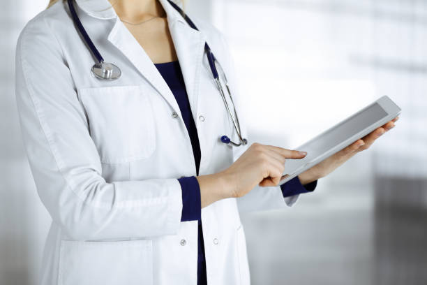 istock Unknown woman-doctor is holding a tablet computer in her hands, while standing in a clinic cabinet. Female physician at work, close-up. Perfect medical service in a hospital. Medicine concept 1310306273