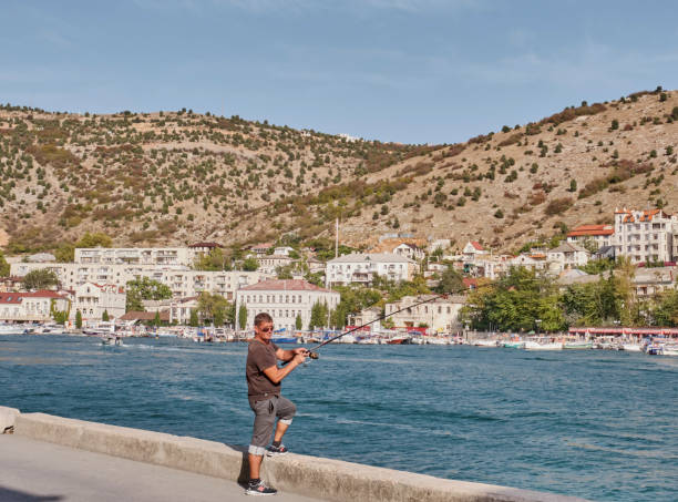 unknown man with a fishing rod on the background of balaklava bay and balaklava town, crimean peninsula. - recreational boat nautical vessel fishing rod motorboat imagens e fotografias de stock