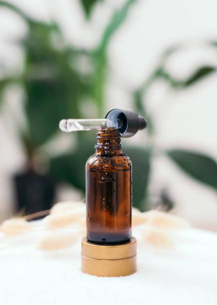 istock Opened brown glass dropper bottle with pipette with black rubber tip on the background of green natural leaves in the bathroom. Skin concept. Organic spa cosmetics. Fashionable concept. 1310310564