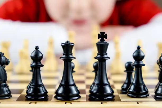 Close-up of some black chess pieces with a girl's face out of focus in the background. Concept of playing chess at home, hobbies at home