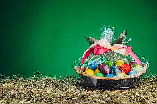 Easter gift basket with multicolor eggs, green background
