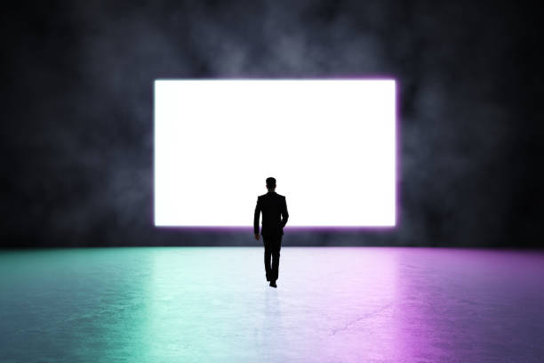 istock Future concept with man silhouette heading to blank white screen in glowing purple led frame on dark wall in empty presentation room with glossy floor in pink shades. Mockup 1310316553