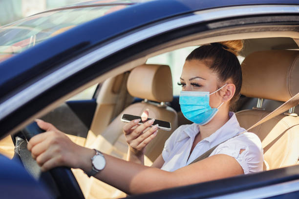 Cute young woman with protective mask driving a car and talking on the phone Cute young woman with protective mask driving a car and talking on the phone during COVID-19 pandemic car rental covid stock pictures, royalty-free photos & images