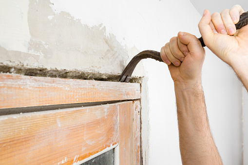 Young adult man hands using crowbar and breaking old wooden door frame from wall. Closeup. Preparing for repair work of home. Side view.