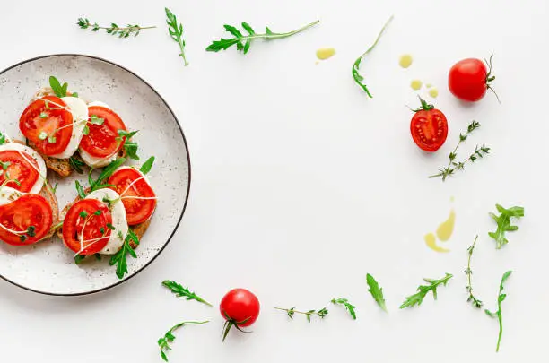 Italian food concept. Open sandwiches with mozzarella, tomatoes and arugula on white plate. Overhead, frame composition
