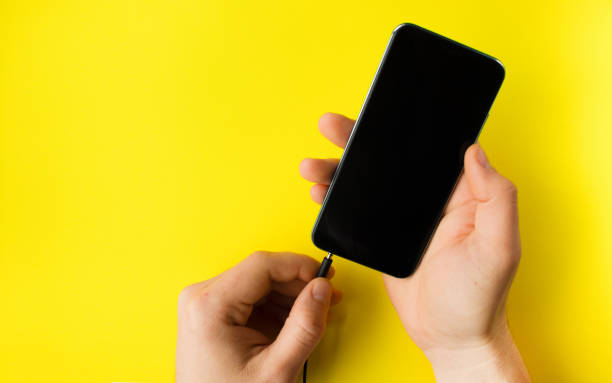 istock The hand holds a smartphone and the second inserts the cable on yellow background 1310322096
