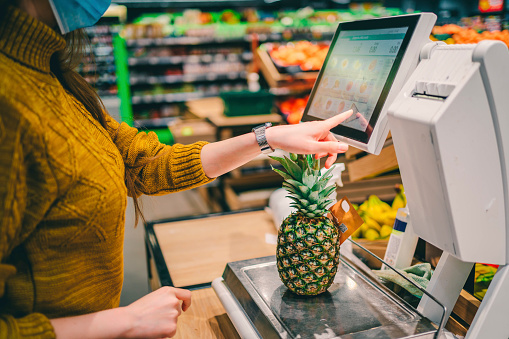 Young woman in the supermarket measuring pineapple on digital scale