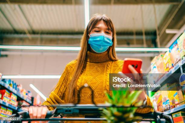 Woman Checking Shopping List On Smartphone Stock Photo - Download Image Now - Protective Face Mask, Shopping Cart, Supermarket
