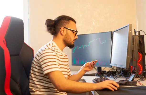 Stockbroker man working with graphs and financial reports on computer screen and working in his modern office.