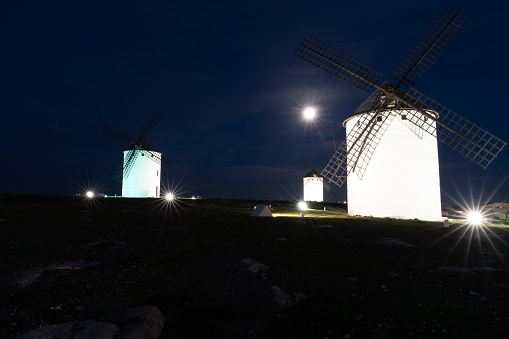 A view of the historic white windmills of La Mancha above the town of Campo de Criptana at night under a full moon