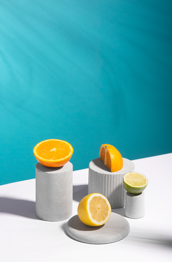 Citrus still life concept with lemon,lime and orange on gray stands and podiums over blue background and hard shadows, vertical