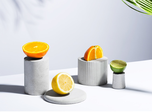 Citrus still life concept with lemon,lime and orange on gray stands and podiums over white background and hard shadows