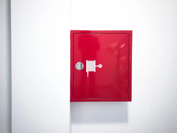 Red fire hose reel cabinet hangs on wall. Firefighting equipment
