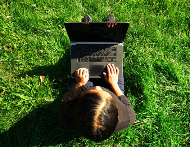 istock Young black woman sitting on the grass with her computer working 1310336725