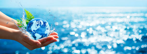 environment concept - hands holding globe glass in blue ocean with defocused lights - environment nature water globe imagens e fotografias de stock