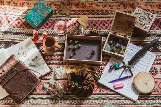 Overhead view of role-playing game equipment, like a dice bag, pieces of paper, notebooks, crystals a pen, and an eraser on a colorful plaid. Edited in a vintage style
