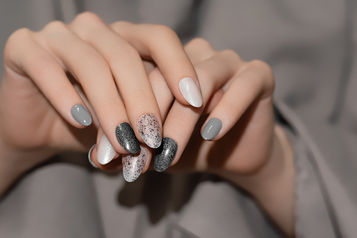 Female hands with beige nail design. Glitter gray nail polish manicure. Woman hands on gray fabric background.