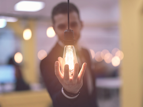 businessman at office holding a hand around light bulb representing concept of business solutions idea and green energy