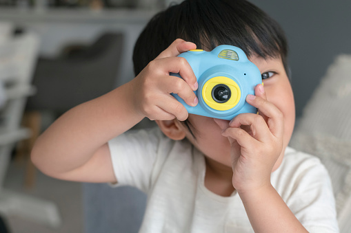 An adorable preschool age boy of Asian descent pretends to take a photograph with a toy camera. Imaginative play, creativity, learning and childhood development concepts.