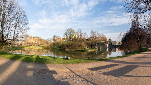 Dresden, Zwingerteich on a sunny springtime day with a lot of people relaxing on the green grass. The back of the Semper Opera House is in the background.