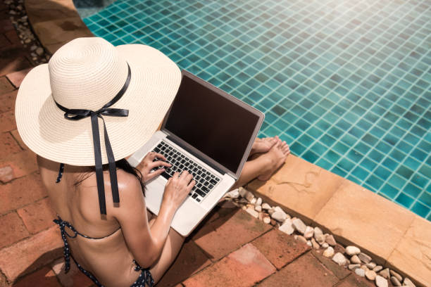 istock Asian Young Woman using her laptop with big hat on poolside edge on sunny day 1310358579