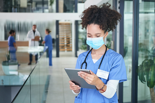 Cropped shot of an attractive young nurse standing and wearing a face mask while using a digital tablet