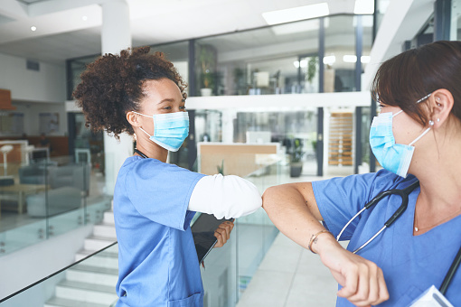 Cropped shot of an attractive young nurse standing and elbow bumping a coworker as a greeting in the clinic