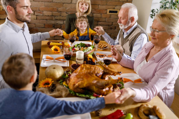 istock Extended family praying before Thanksgiving dinner at dining table. 1310383539