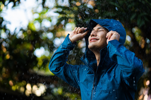 Young Asian man in raincoat in the outdoor with rain and clouds.