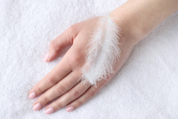 Soft white feather lying on woman hand closeup. Hand skin care concept
