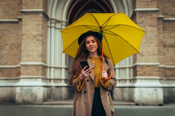 istock Woman using smartphone and holding a yellow umbrella 1310387343
