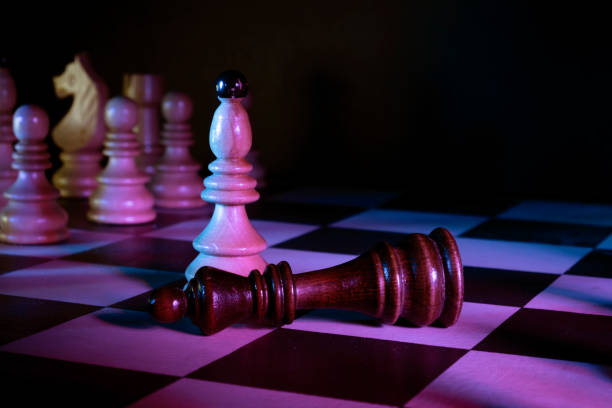 istock Chess pieces, on a chessboard. Dark king laying down defeated. Dark background, neon studio lights. 1310389605