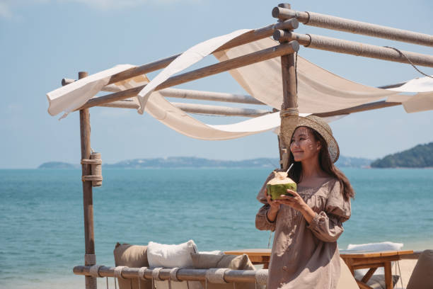 a beautiful young asian woman holding and drinking coconut juice on the beach