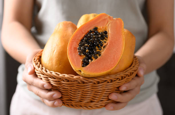 fruta de papaya madura en una cesta sosteniendo de la mano de la mujer - papaya fruta tropical fotografías e imágenes de stock