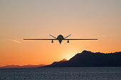 Silhouette of spy drone flying over  sea (UAV) and on background beautiful view of sun hiding behind  surface of mountain