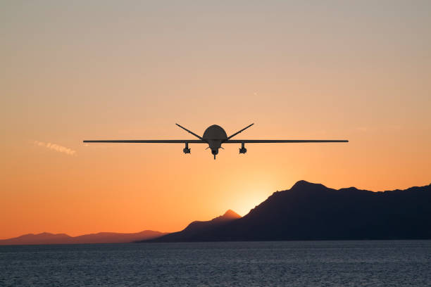 Silhouette of spy drone flying over  sea (UAV) and on background beautiful view of sun hiding behind  surface of mountain stock photo