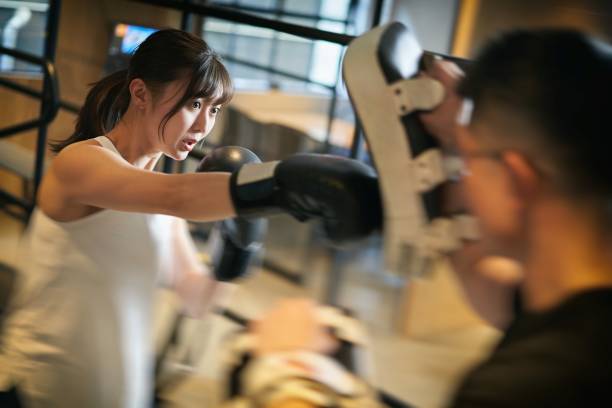 asiatische frau lernt kickboxen von einem personal trainer - fist women punching asian ethnicity stock-fotos und bilder