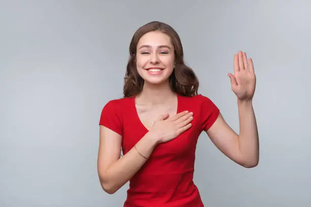 Photo of Swear to say truth. Sincere happy young brunette woman, raising palm and holding hand on chest, promising to me honest