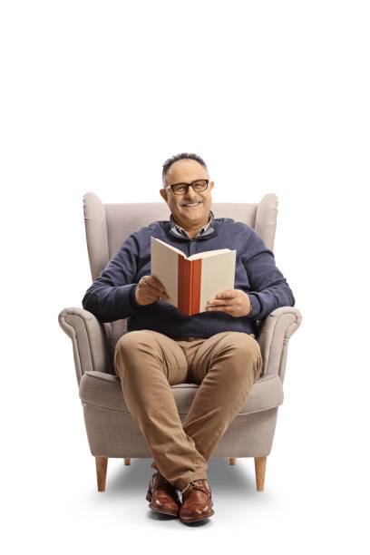 Smiling mature man sitting in an armchair and reading a book Smiling mature man sitting in an armchair and reading a book isolated on white background chubby arab stock pictures, royalty-free photos & images