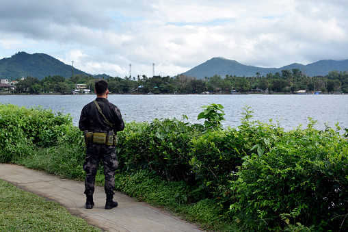 Sampaloc Lake, San Pablo City, Laguna, Philippines - February 28, 2021: Fully armed, uniformed military personnel patrolling lake perimeter road during Covid 19 pandemic general quarantine.