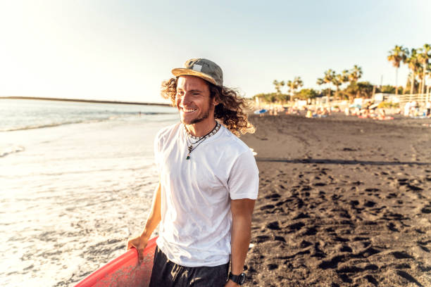 szczęśliwy przystojny mężczyzna bawiący się, chodzący z deską surfingową na plaży. - surfing surf wave men zdjęcia i obrazy z banku zdjęć