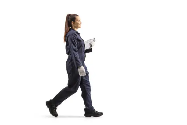 Full length portrait of a female worker in a uniform walking and holding a clipboard isolated on white background