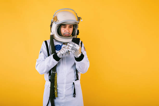Male cosmonaut in space suit and helmet, talking on the mobile phone, on yellow background. stock photo