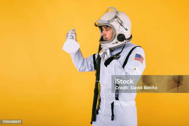 Male Cosmonaut In Spacesuit And Helmet Holding A Fpp2 Mask On Yellow Background Covid19 And Virus Concept Stock Photo - Download Image Now