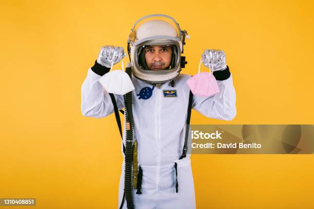Male Cosmonaut In Spacesuit And Helmet Holding Two Fpp2 Masks On Yellow Background Covid19 And Virus Concept Stock Photo - Download Image Now