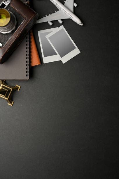 Top view of dark creative flat lay workspace with camera, photo card frame, notebook, travel items and copy space