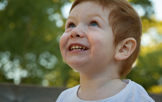 Portrait of a cute, redhead, blue-eyed boy wearing a white t-shirt in a playground on a sunny day