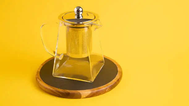 Transparent square teapot with a strainer on a black board on a yellow background. Modern glass teapot. High quality photo